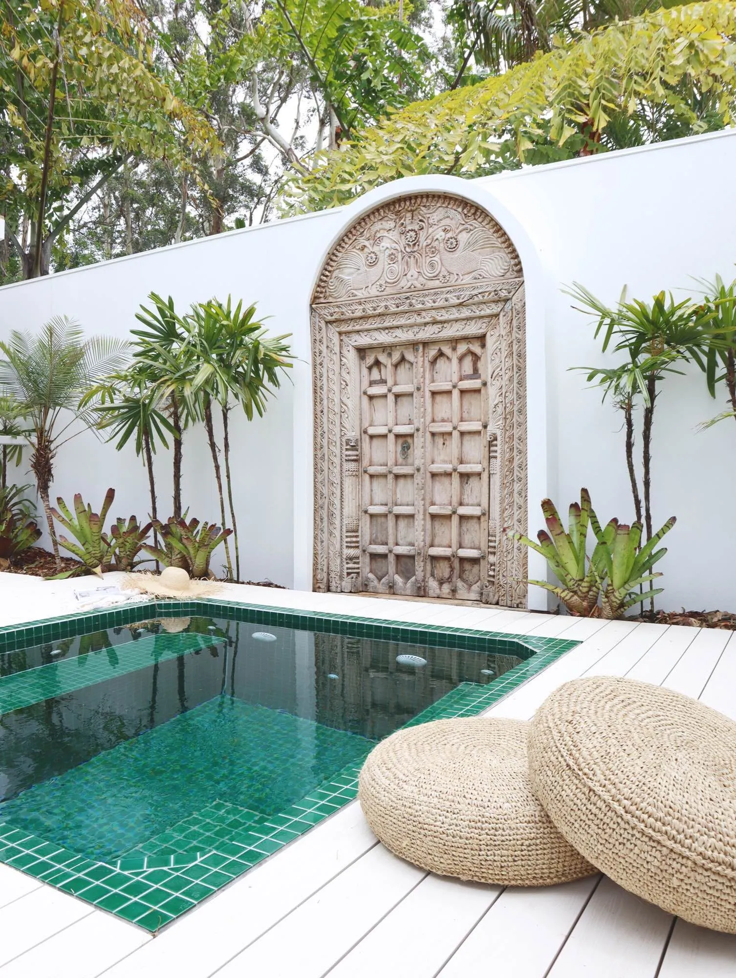 Green-tiled plunge pool in front of a carved timber door feature