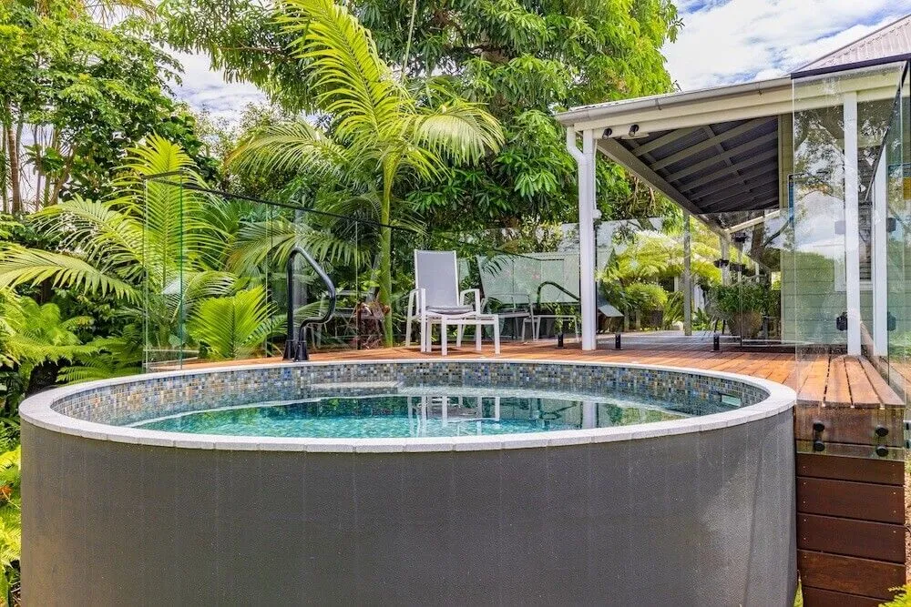 Round grey plunge pool with mosaic trim beside a tropical deck