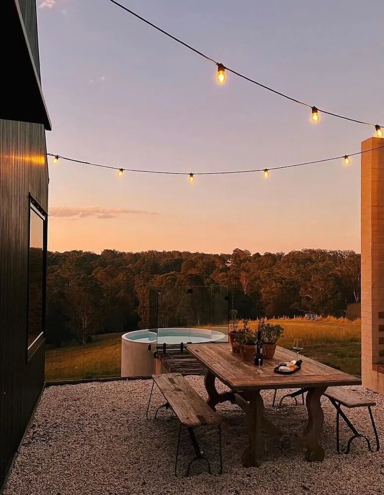 Round plunge pool and outdoor dining table at dusk under festoon lights