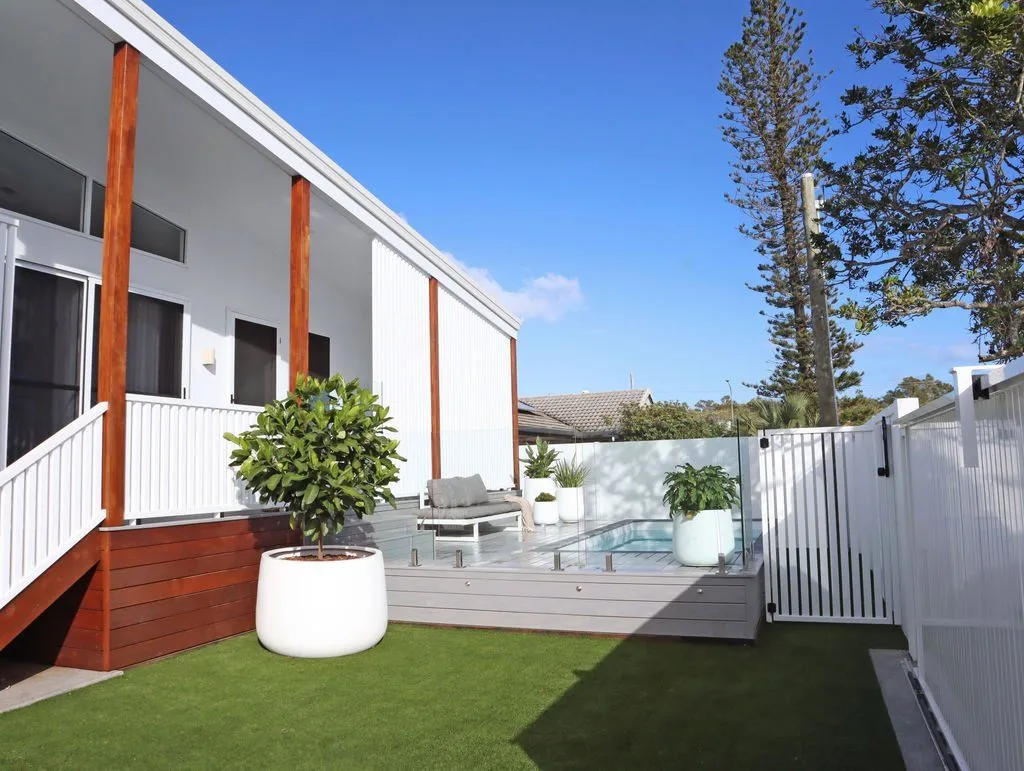 Plunge pool on a raised deck behind white fencing beside a home and lawn