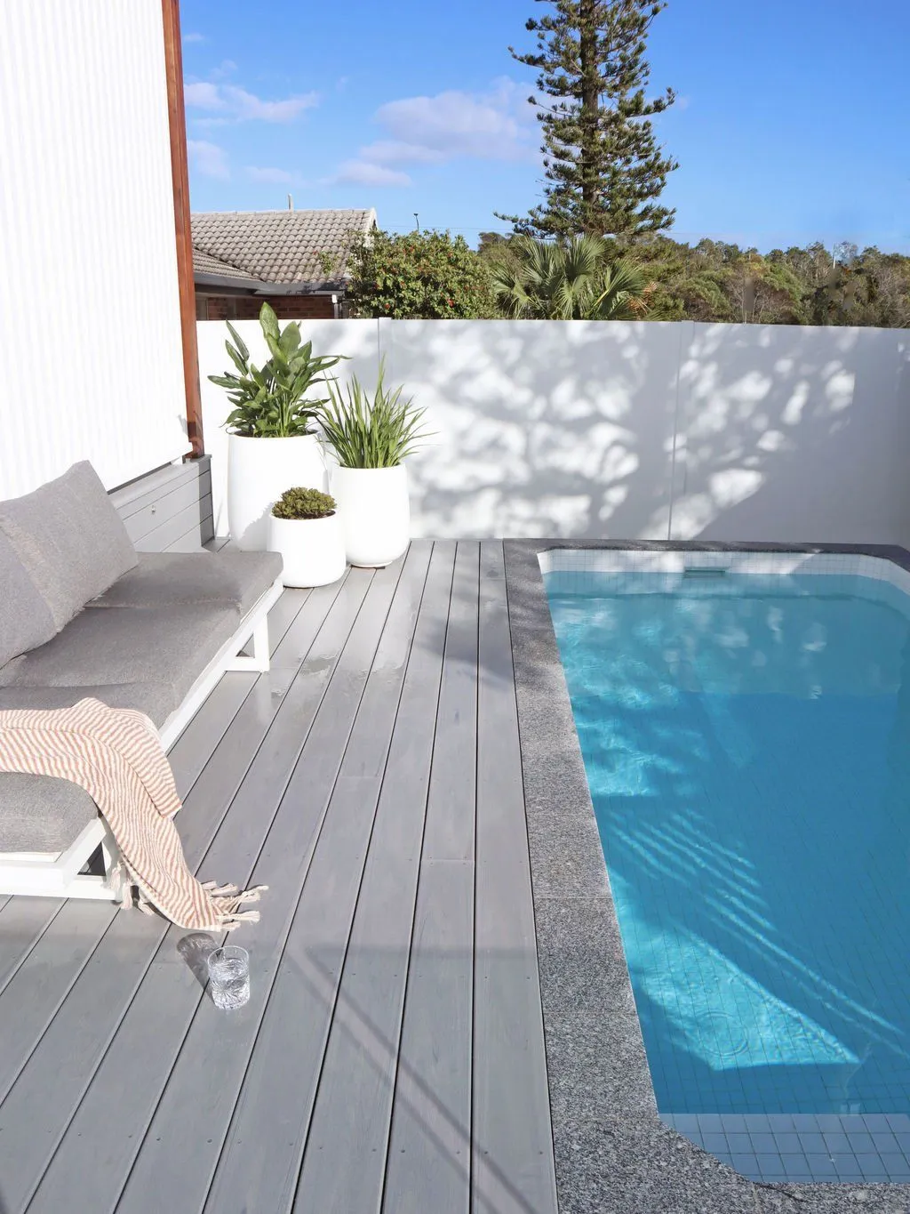 Narrow rectangular plunge pool beside a grey timber deck and outdoor lounge