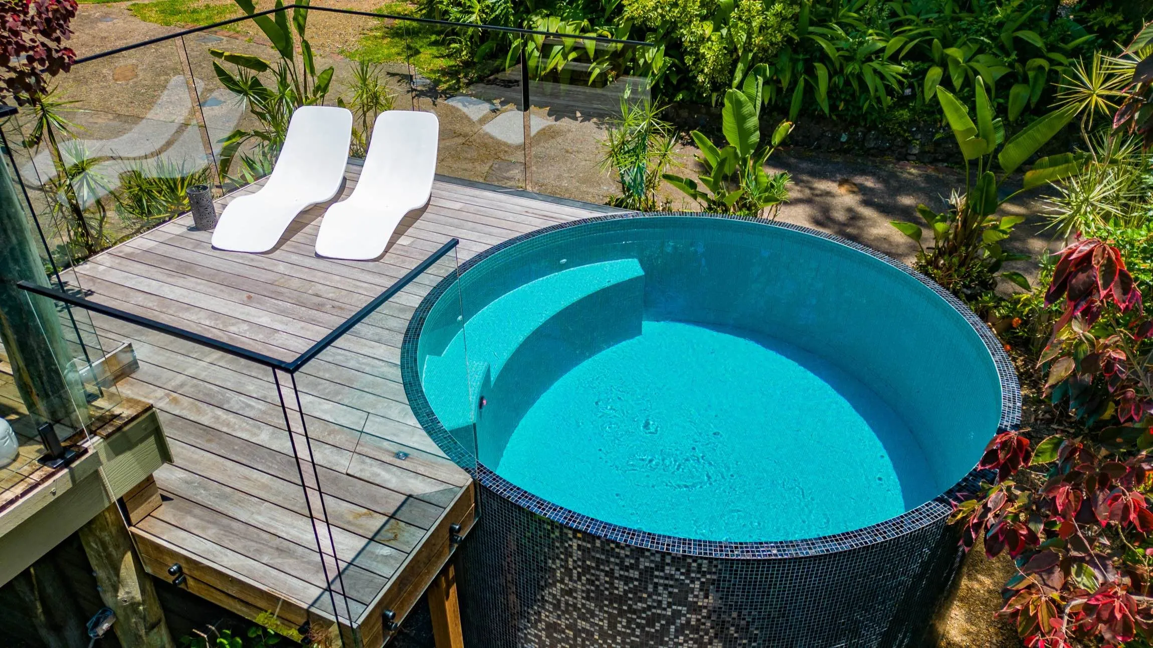 Round dark-tiled plunge pool beside a timber deck and two lounges