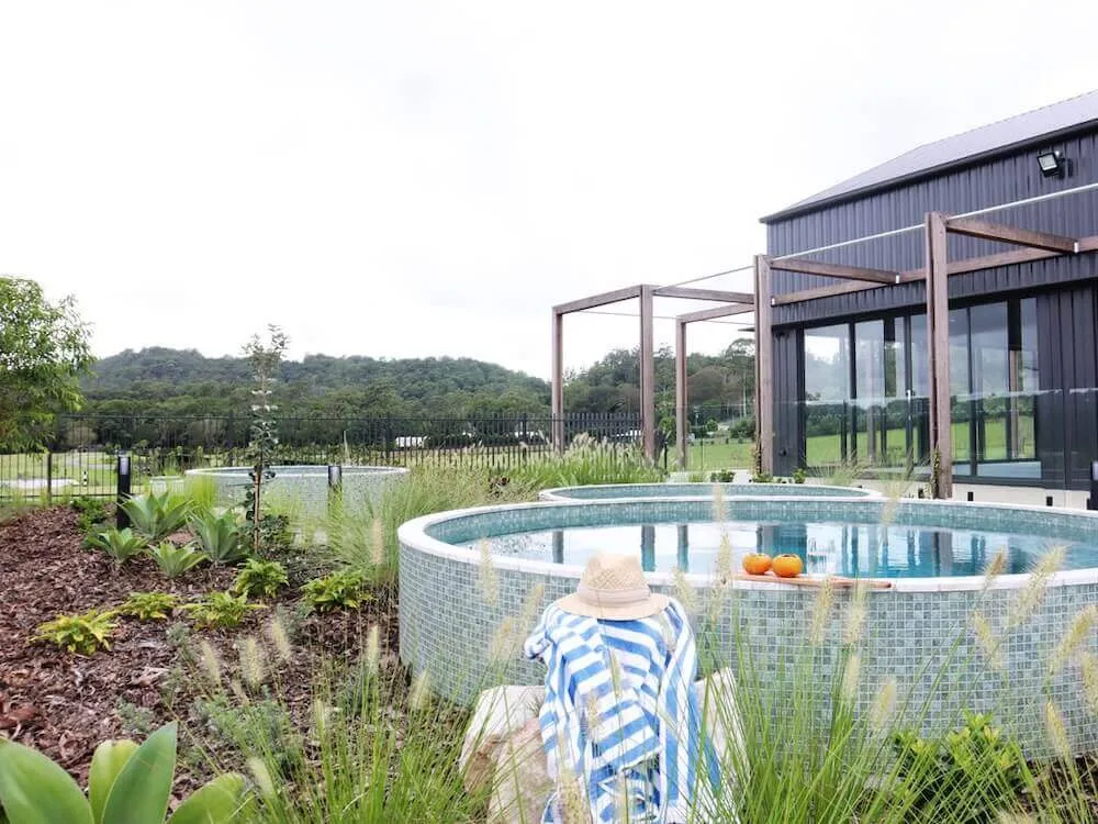 Round mosaic-tiled plunge pool with a striped towel beside a modern home