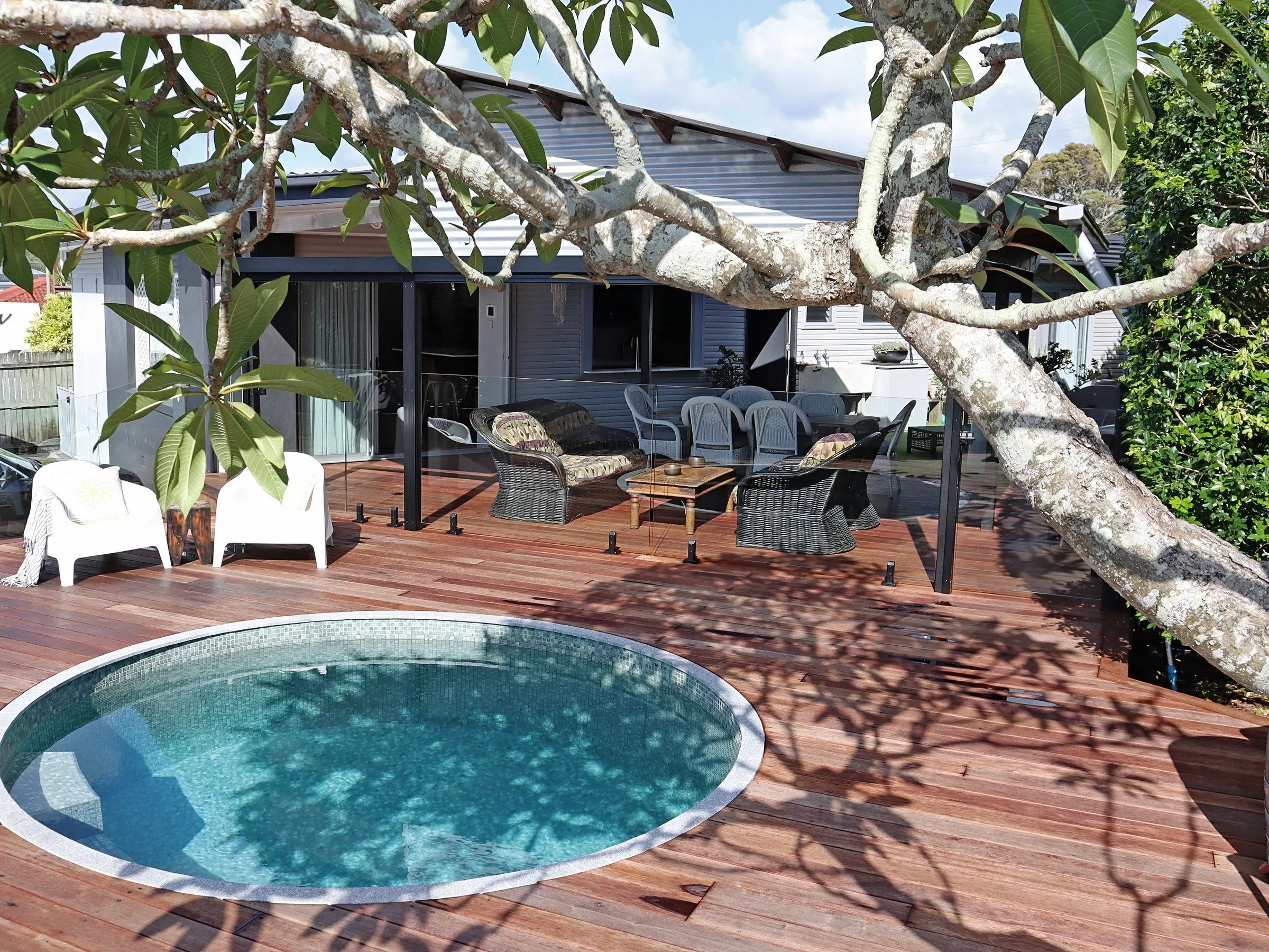 Round plunge pool set into a timber deck under a frangipani tree beside a home