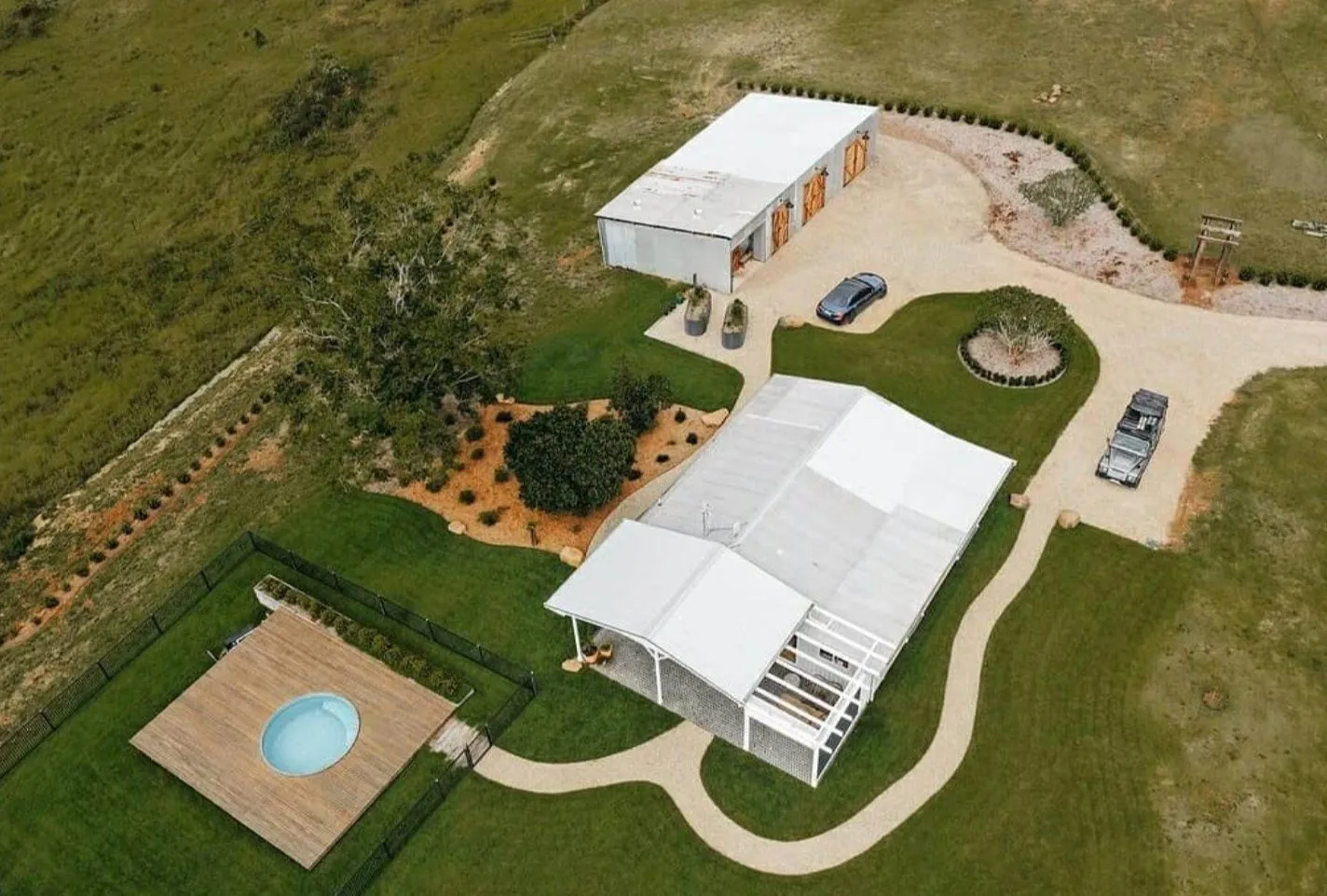 Aerial view of a round plunge pool on a timber deck beside a rural home