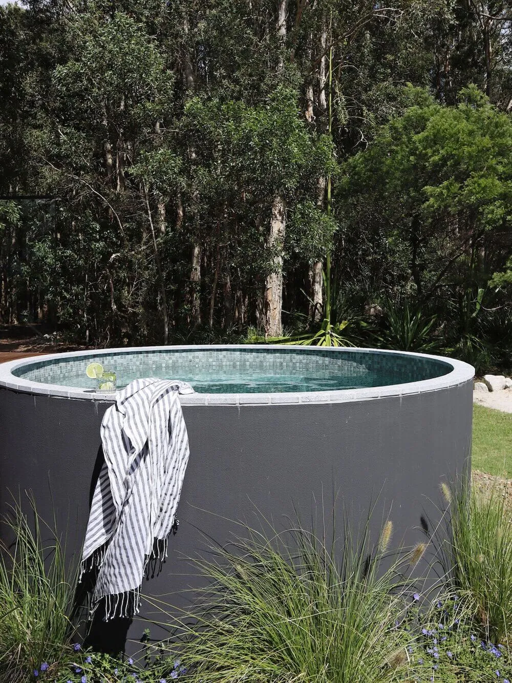 Round grey plunge pool with a striped towel among grasses