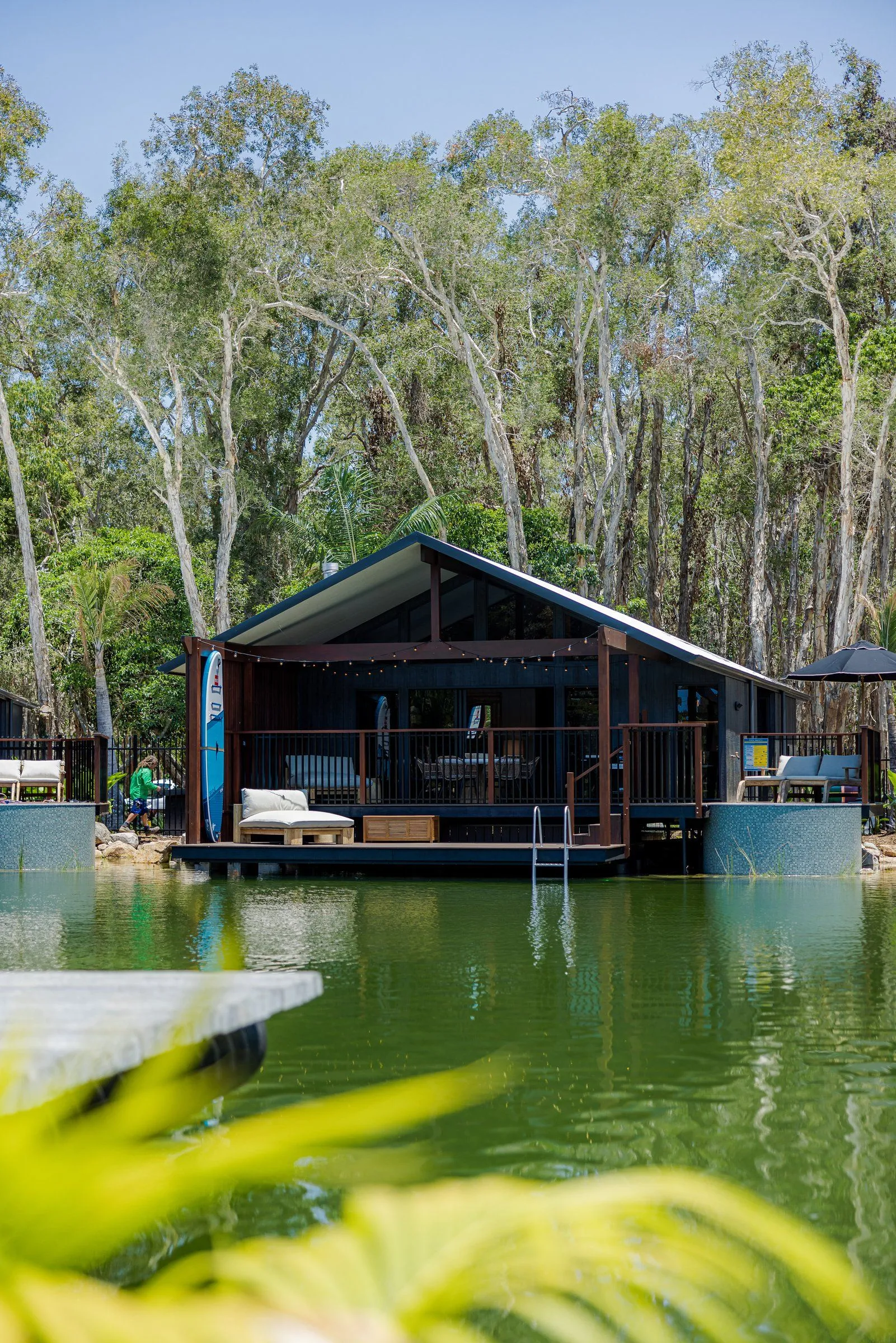 Lakeside cabin with a round plunge pool beside its deck, surrounded by tall trees