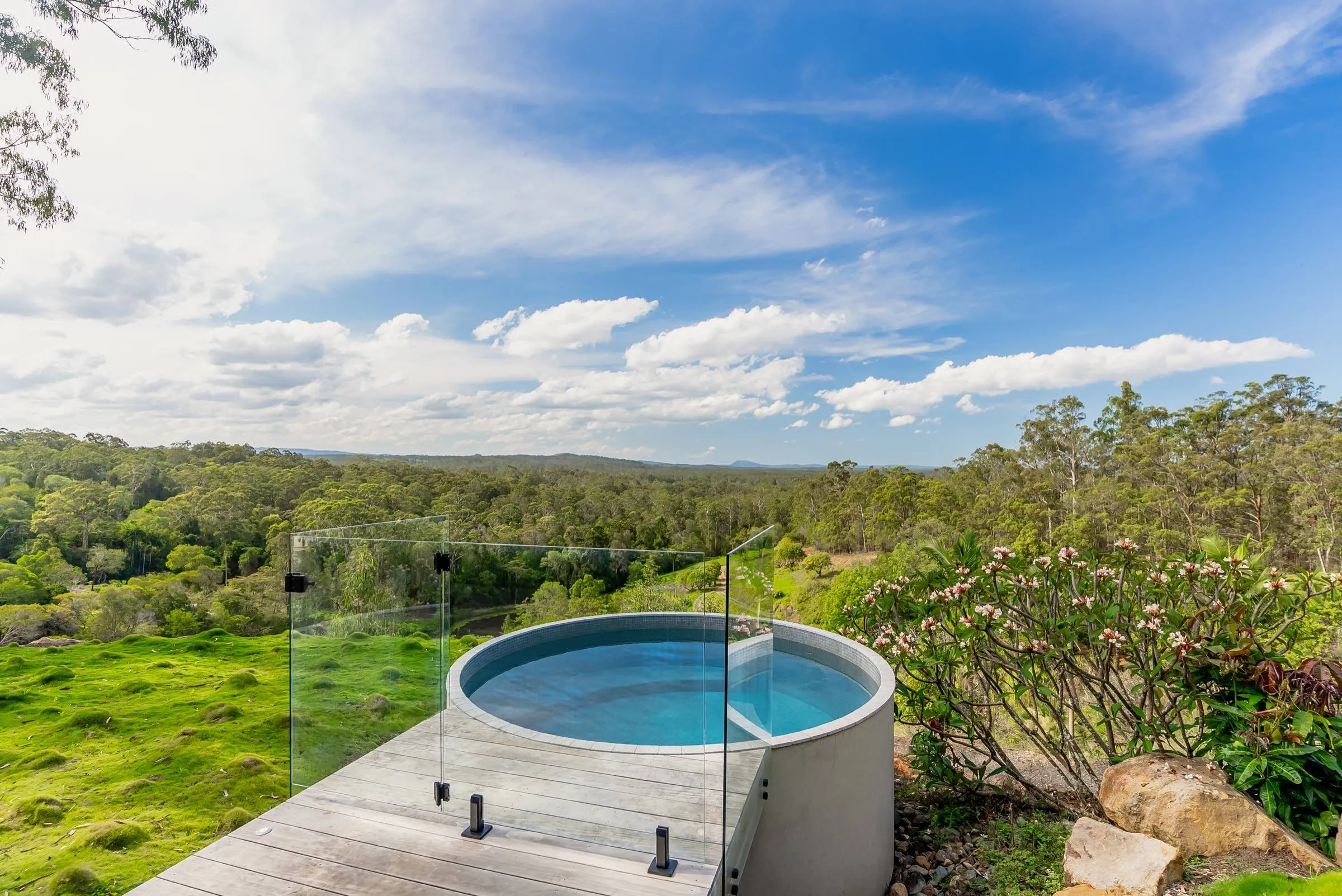 Round plunge pool with glass fencing overlooking green valley views