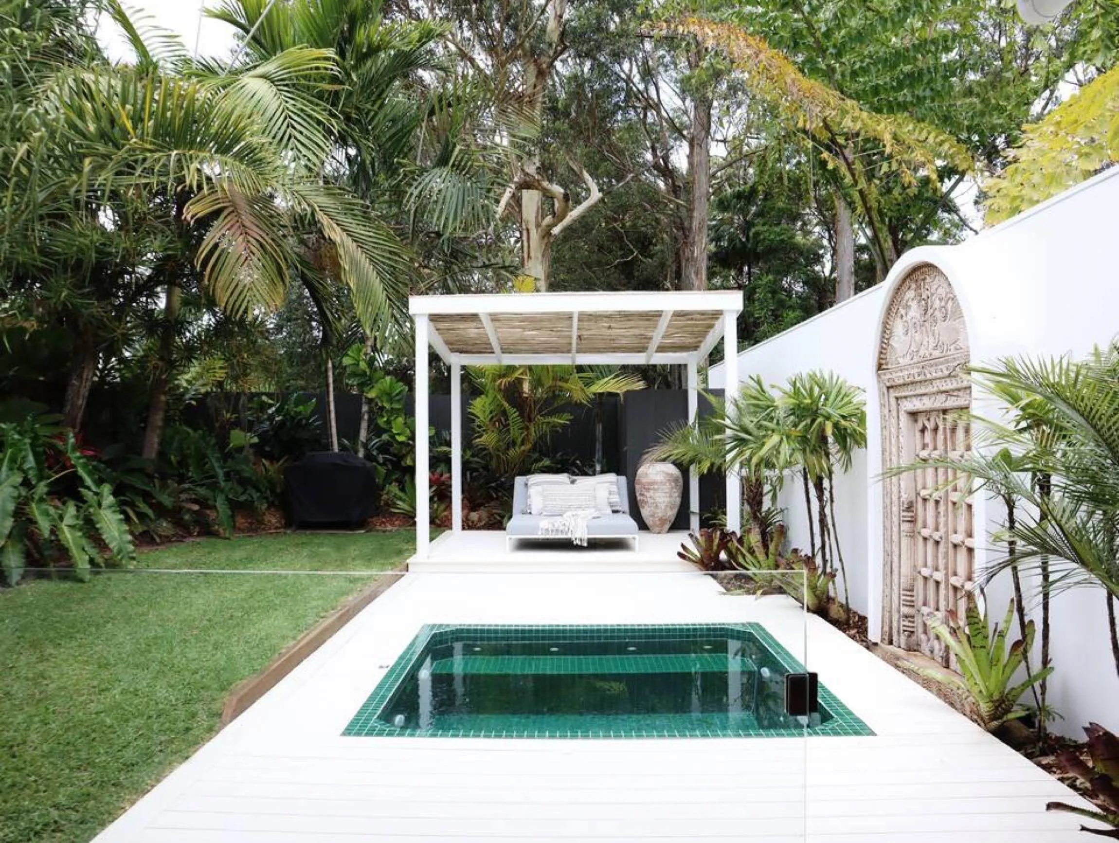 Square green-tiled plunge pool on a white deck beside a pergola