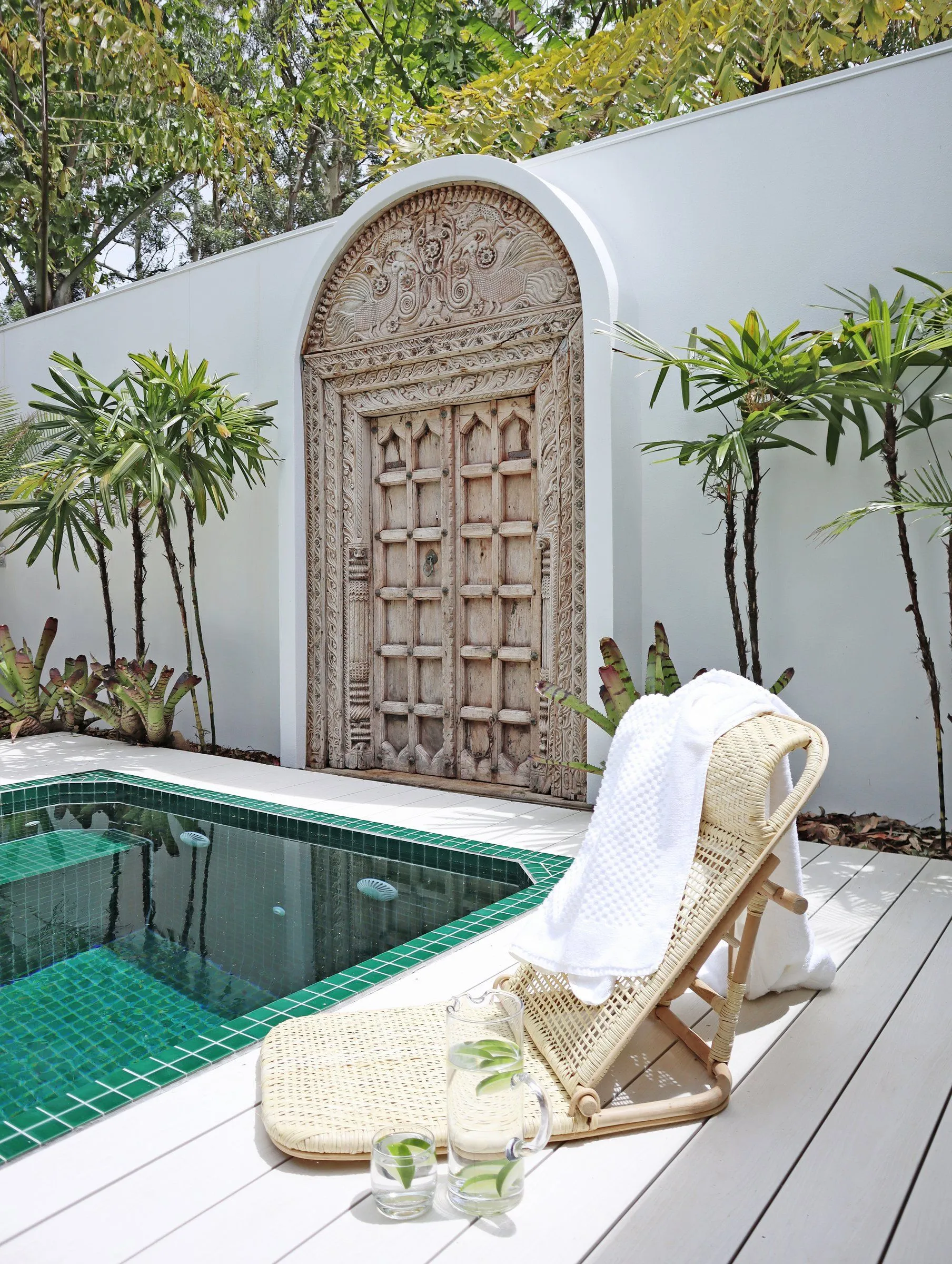 Green-tiled square plunge pool with a deck chair in front of a carved timber door feature
