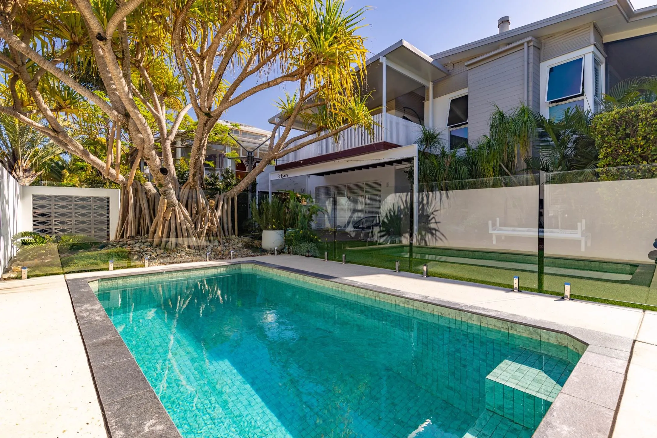 Rectangular plunge pool with glass fencing below a two-storey home