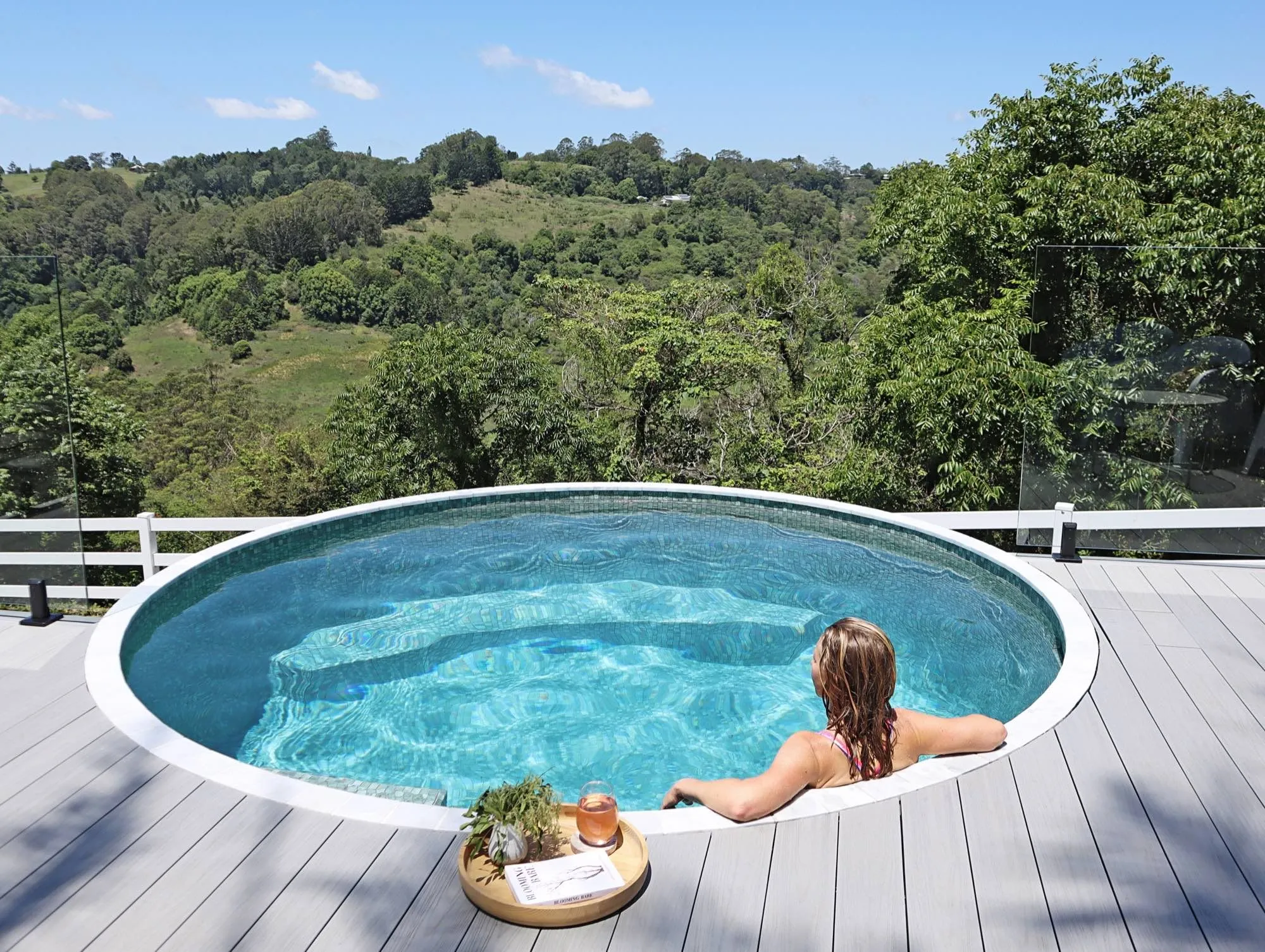 Woman relaxing in a deck-level round plunge pool with hinterland views