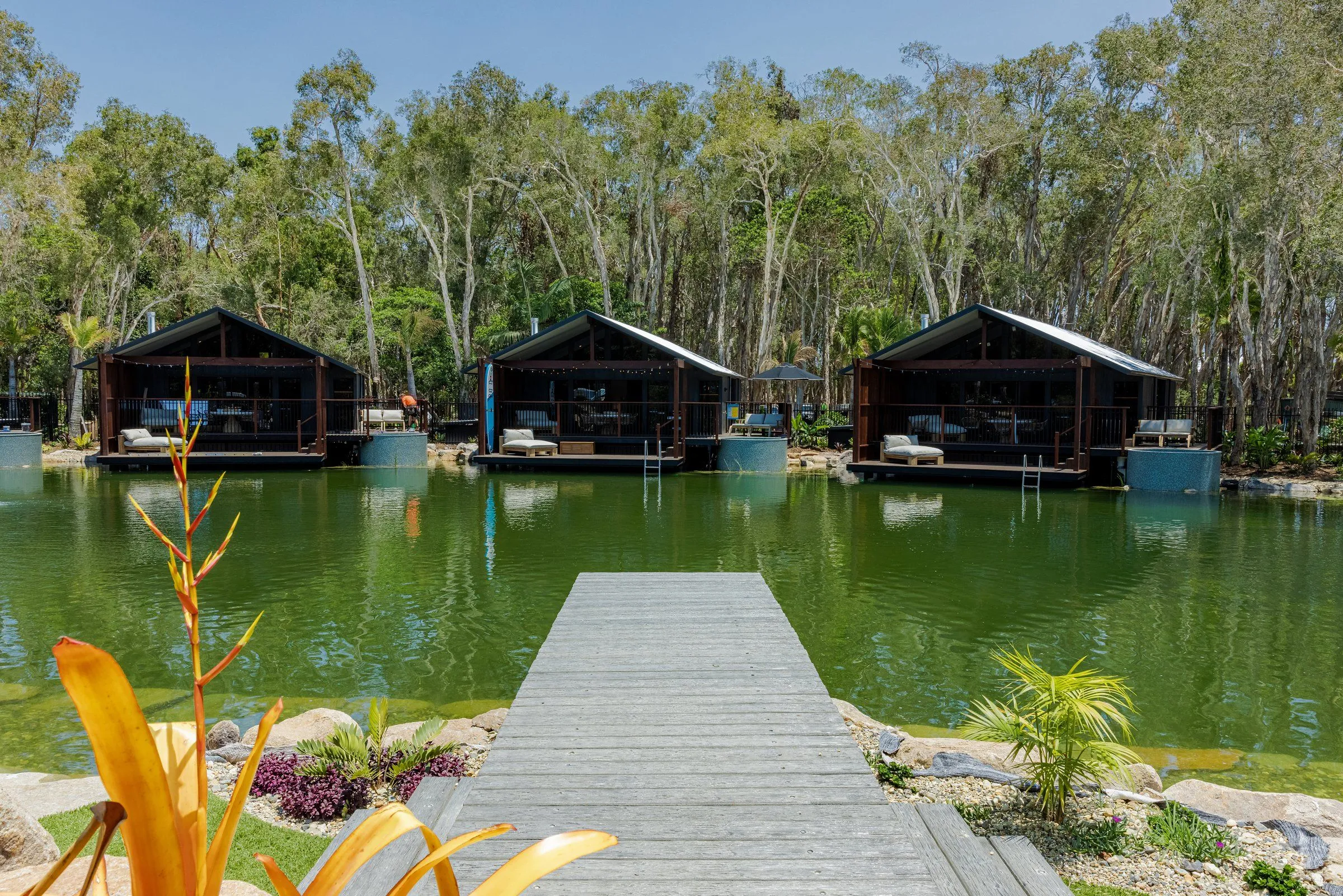 Lakeside cabins with round plunge pools beside their decks, seen from a timber jetty