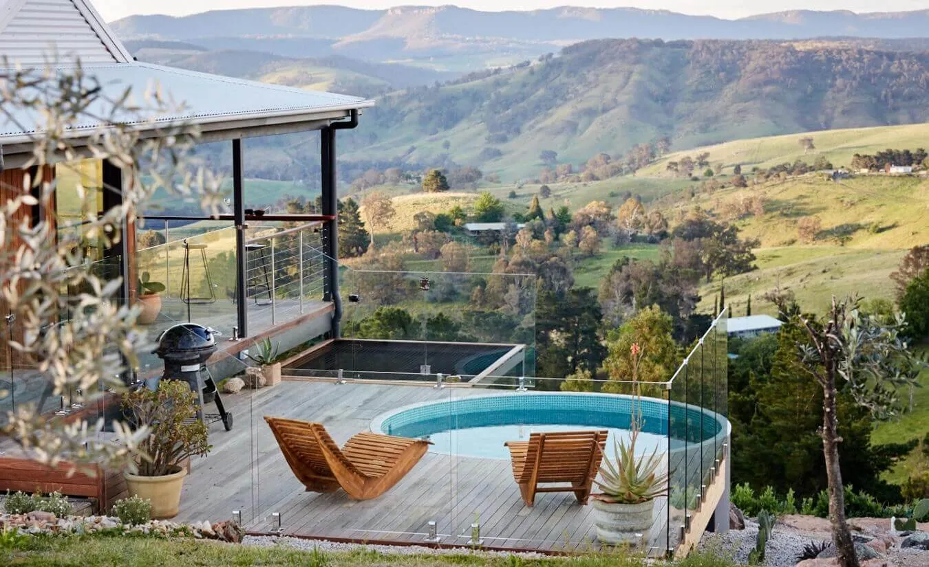 An Eden round plunge pool on a timber deck with two lounge chairs, overlooking a green valley