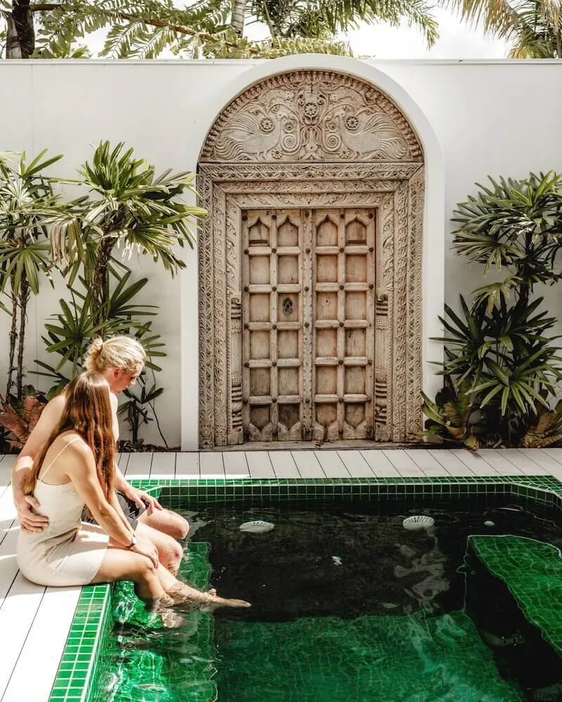 Two women sitting on the edge of a green-tiled plunge pool