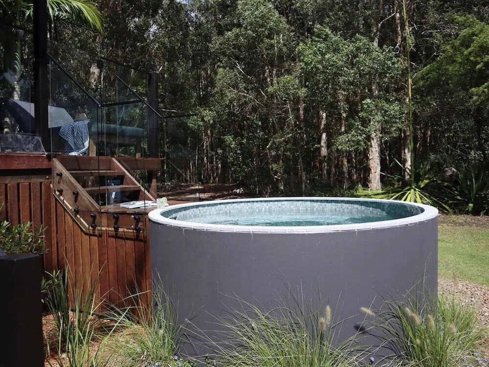 Round grey plunge pool beside a timber deck in bushland