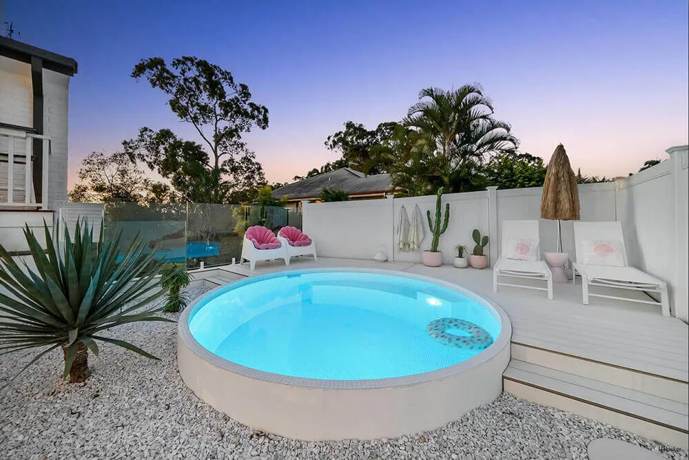 Round white plunge pool glowing at dusk in a gravel courtyard