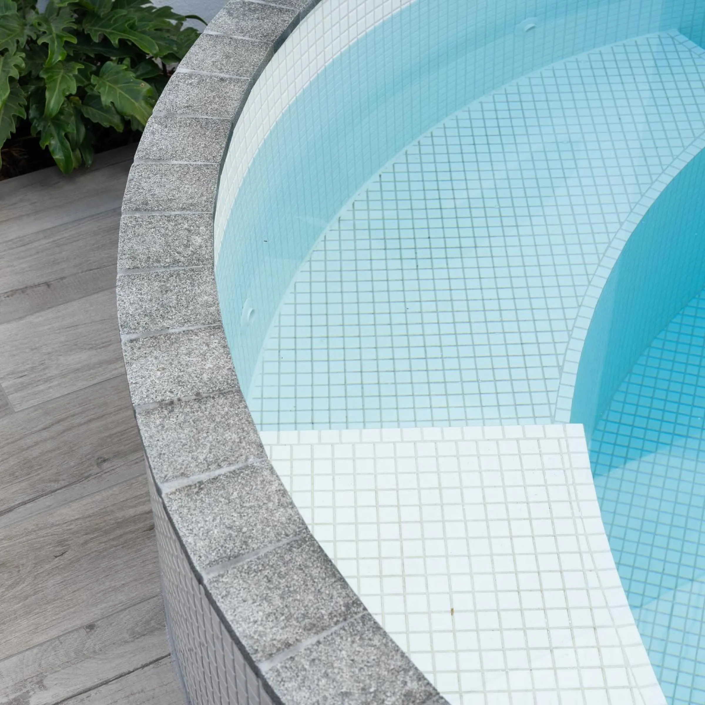 Close-up of white mosaic tiles and coping on a round plunge pool