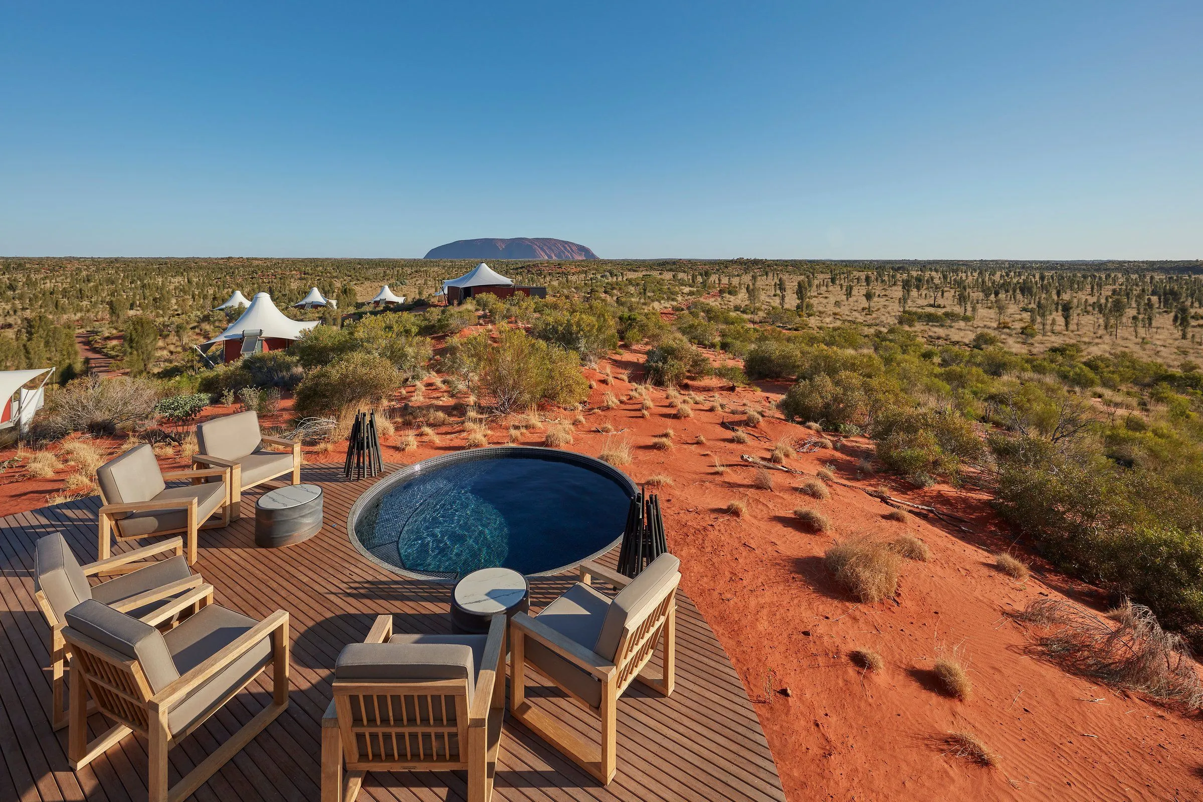 Round plunge pool on a timber deck with outdoor chairs, overlooking the red desert and Uluru