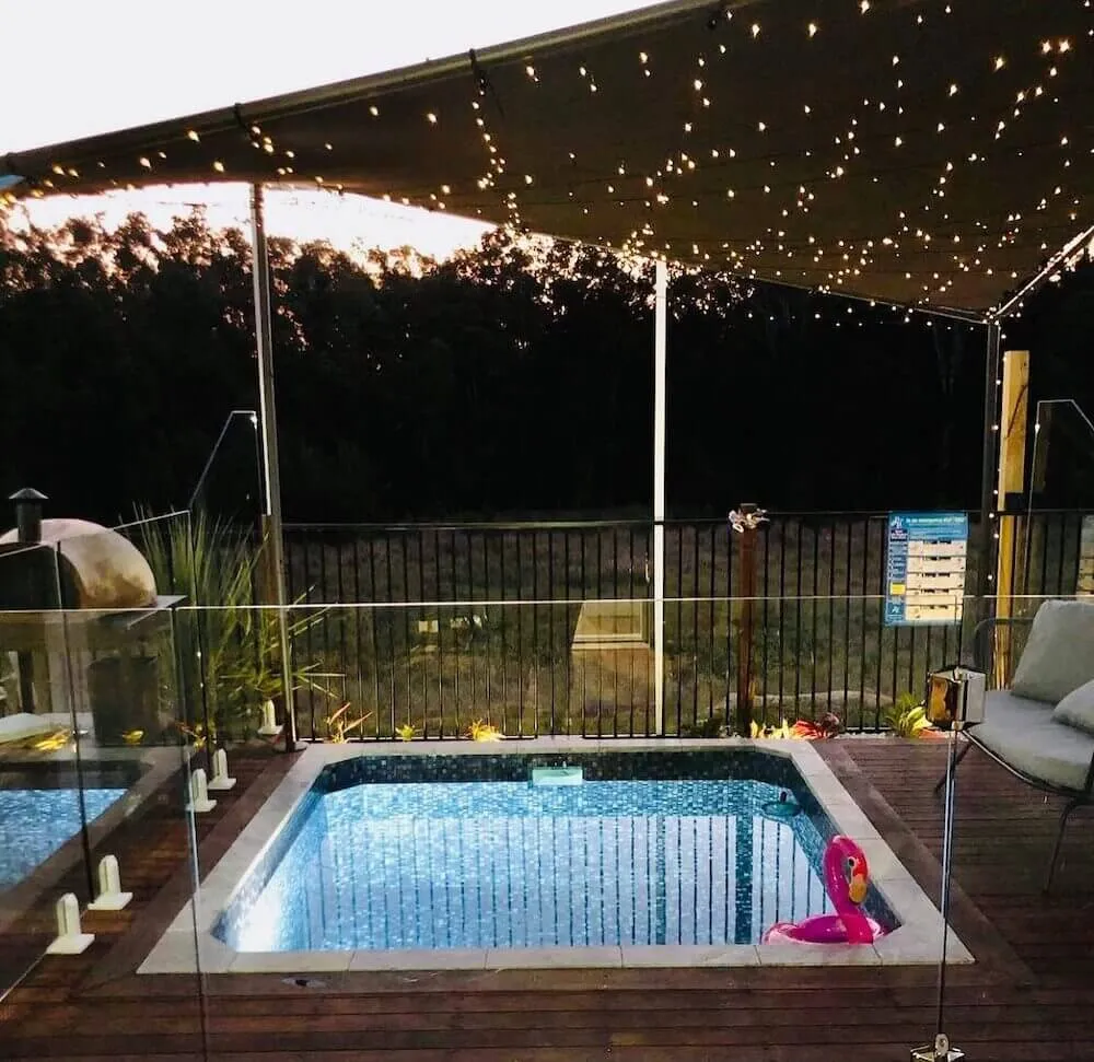 Square plunge pool at night under a shade sail with string lights