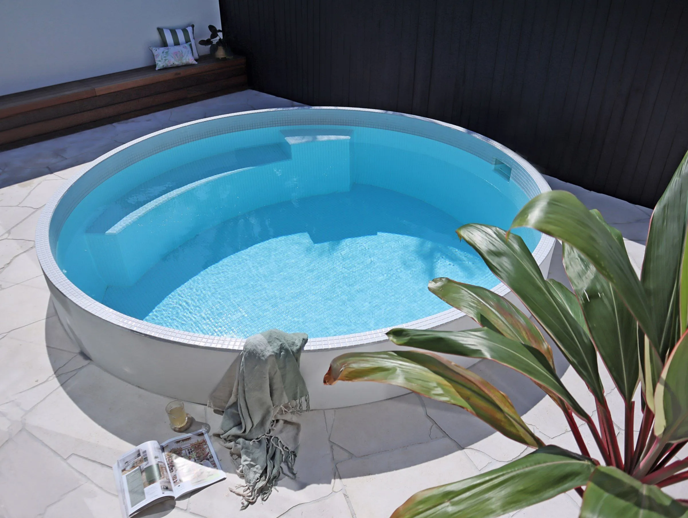 Round white plunge pool on a paved courtyard with tropical plants
