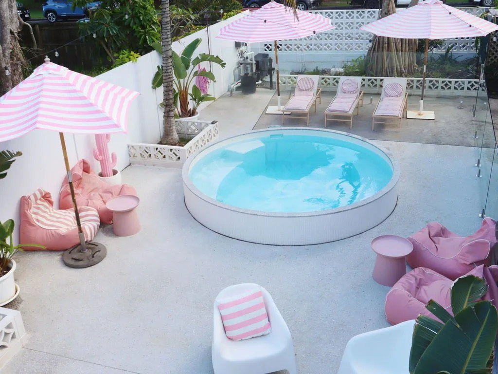 Round white plunge pool on a paved courtyard with pink umbrellas and beanbags