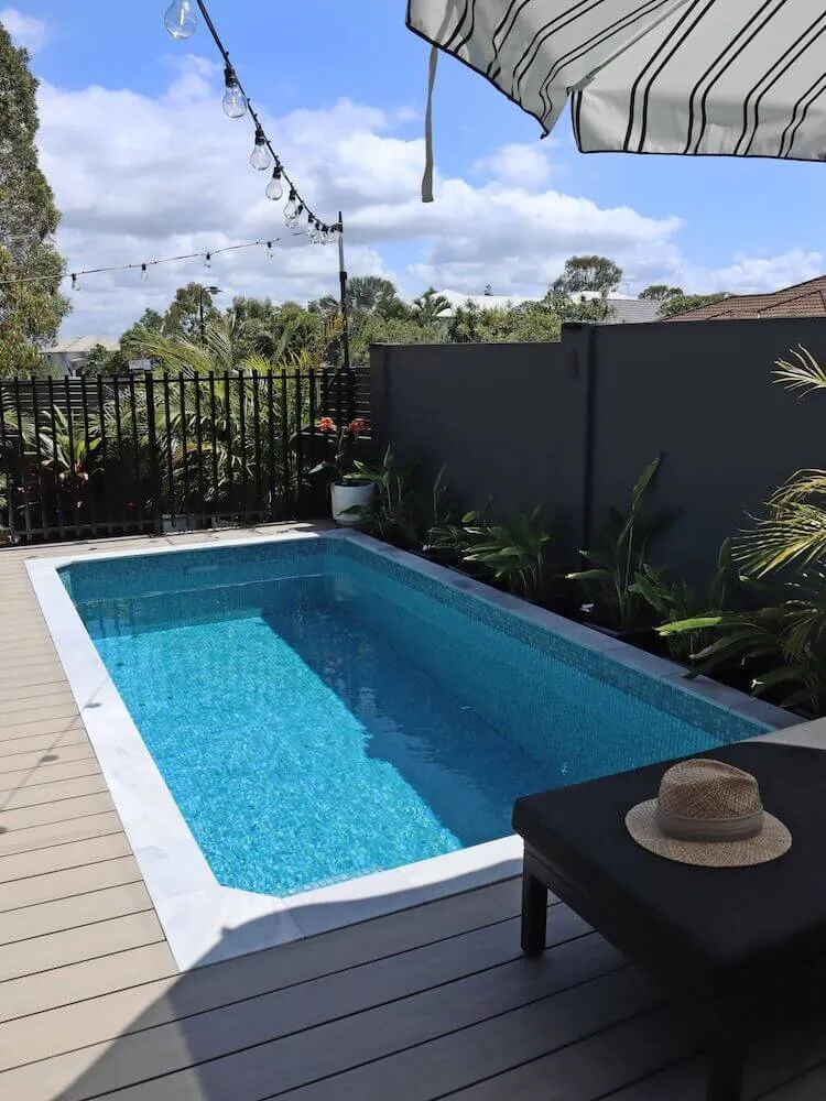 A rectangular Oasis pool set into a timber deck beside a black fence, with a hat on an outdoor table