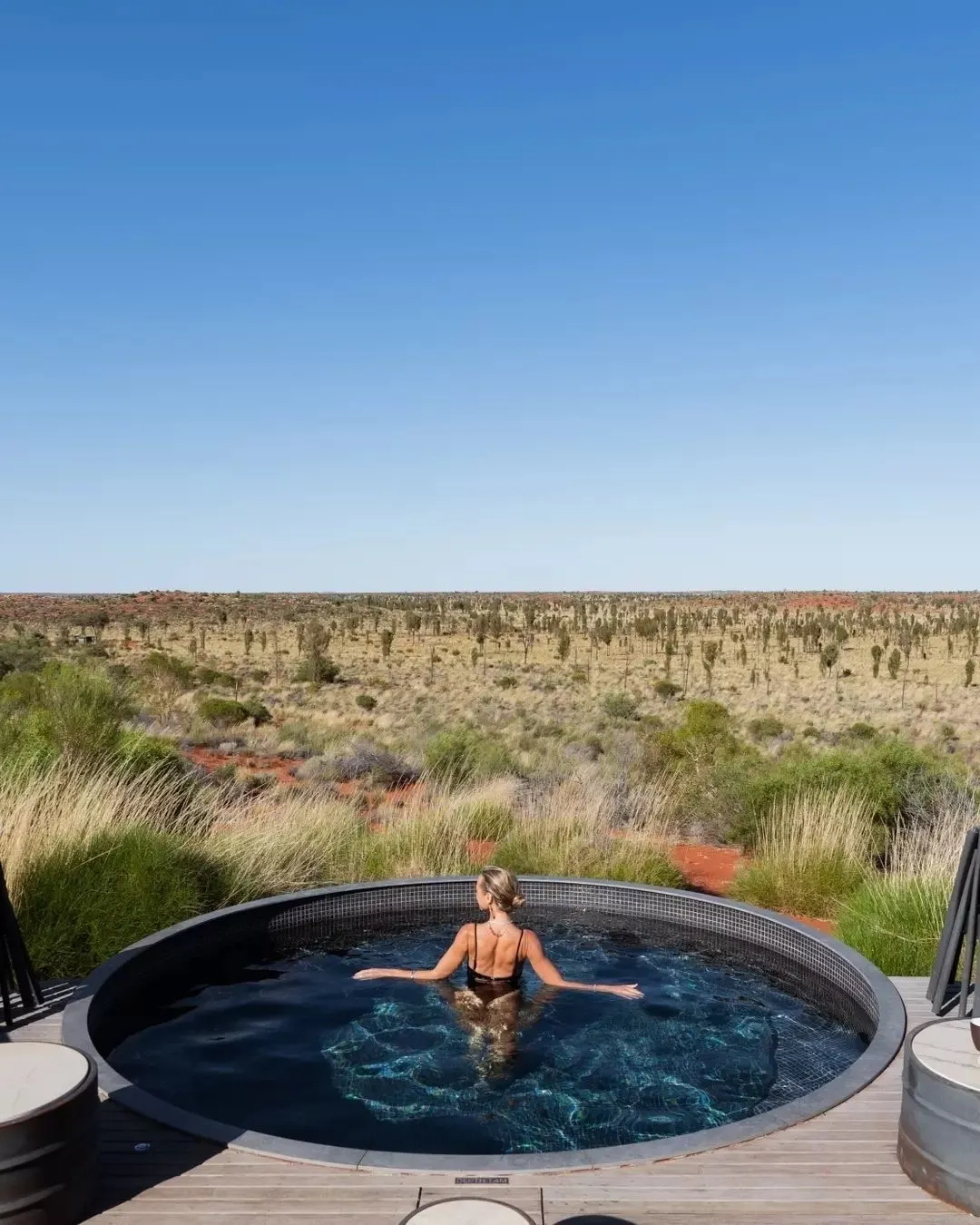 Woman in a dark-tiled round plunge pool overlooking outback scrub