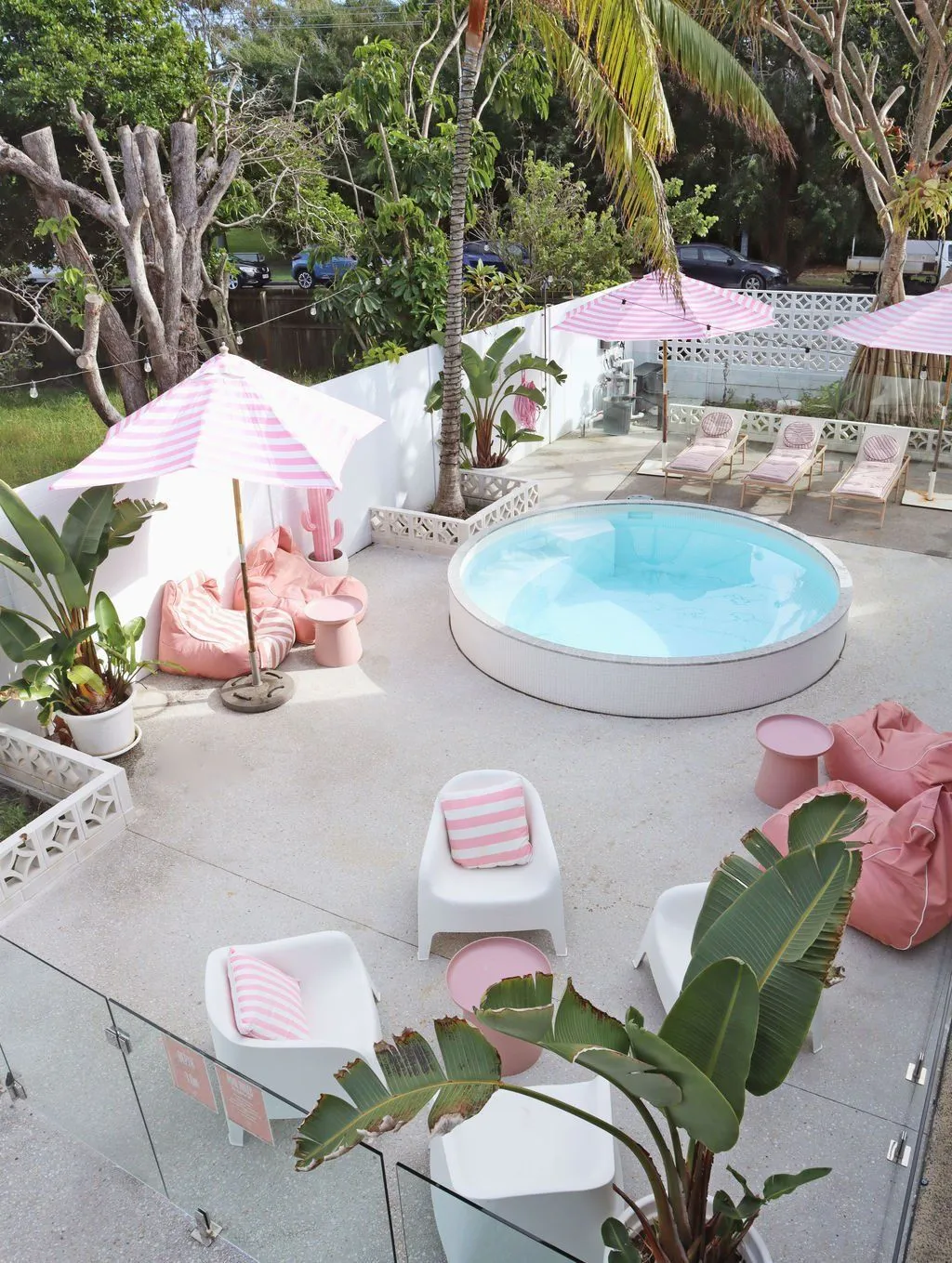 Round plunge pool on a paved courtyard with pink umbrellas, seen from above