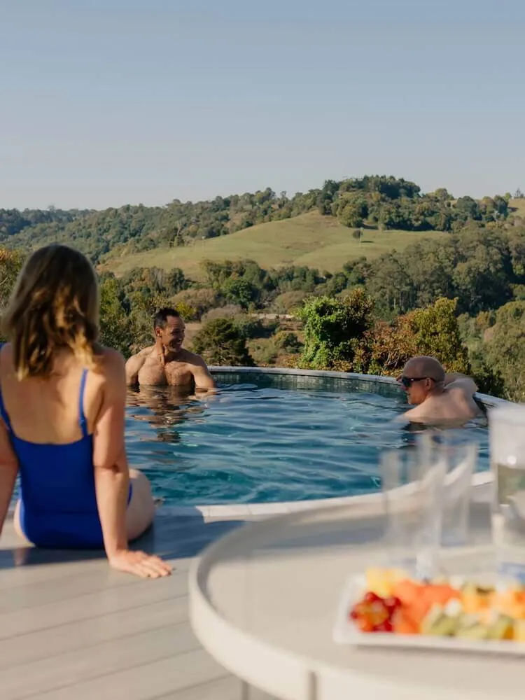 People relaxing in a round plunge pool overlooking green hills