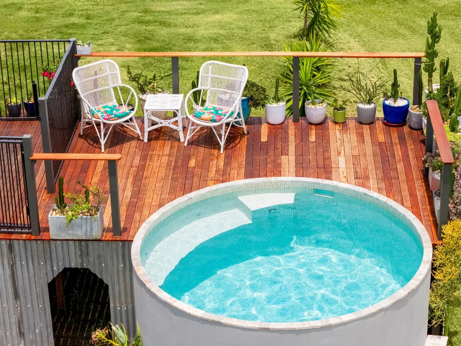 Looking down on a round Haven plunge pool beside a timber deck with white garden chairs