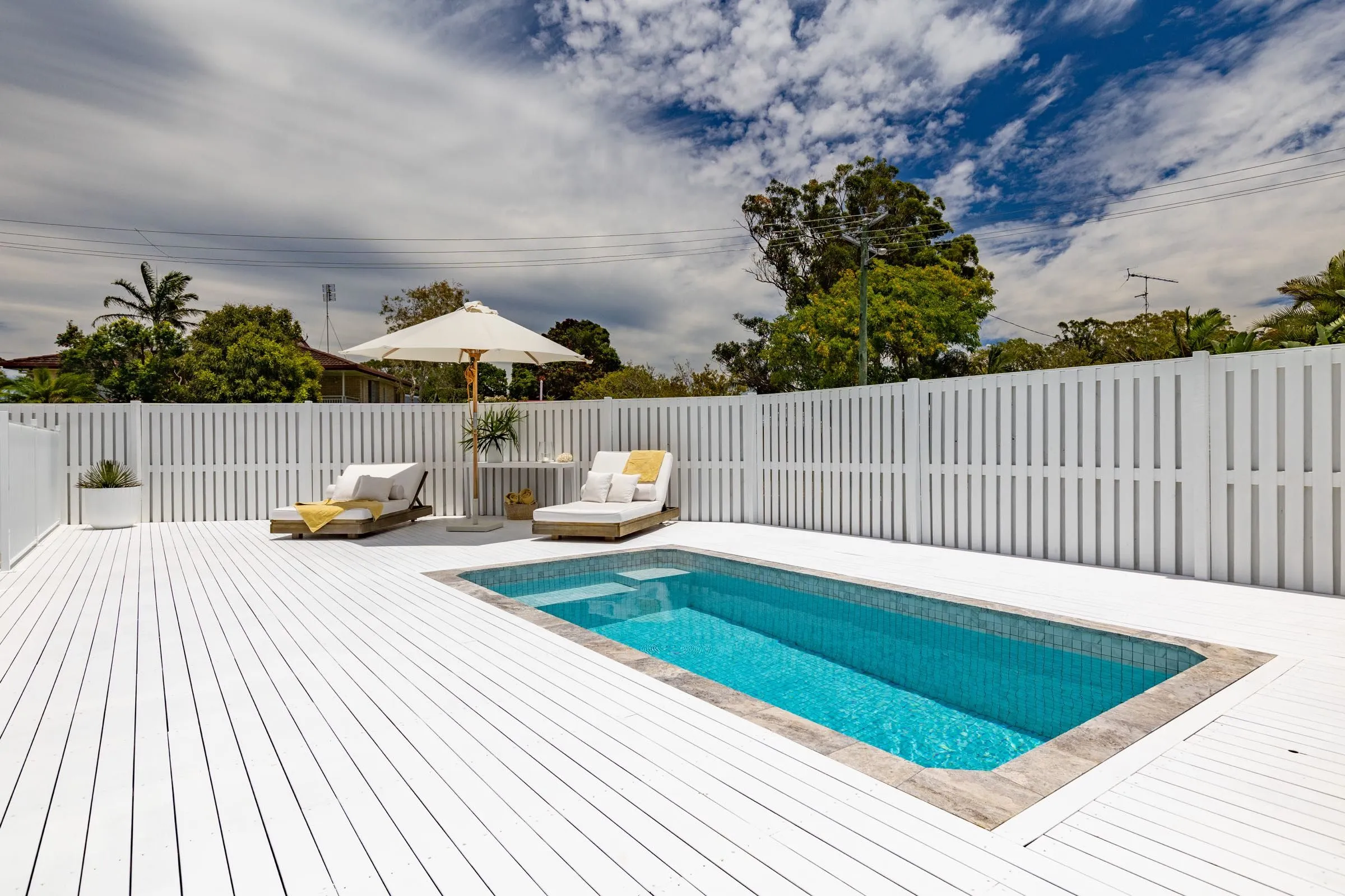 Rectangular plunge pool set into a white deck with sun lounges