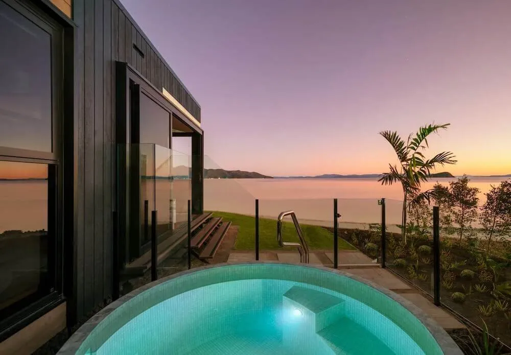 Round plunge pool at dusk beside a black cabin overlooking the water
