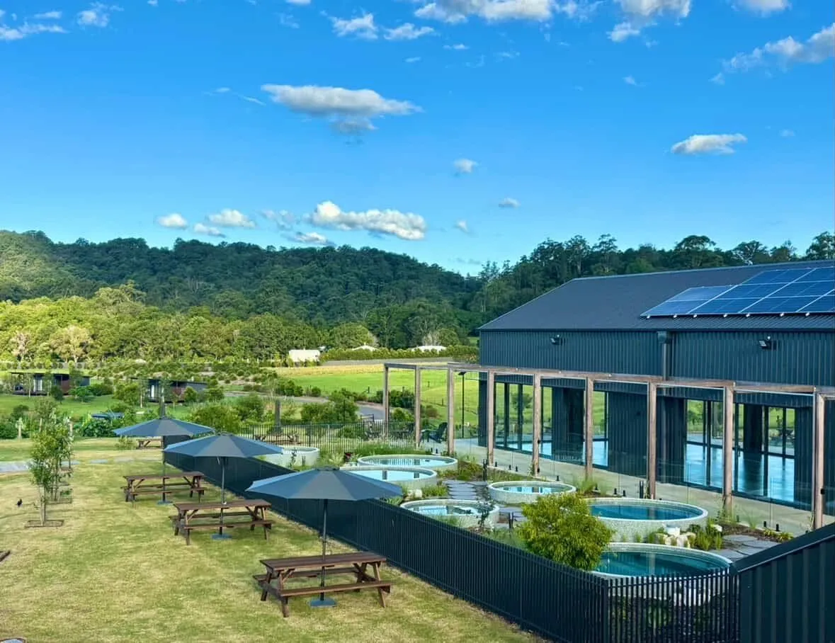 Aerial view of round plunge pools set into a lawn beside a large building, with hills behind