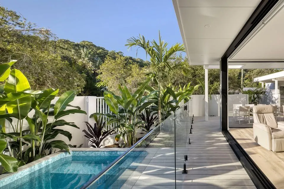 Rectangular plunge pool with glass fencing beside a living area that opens onto tropical gardens