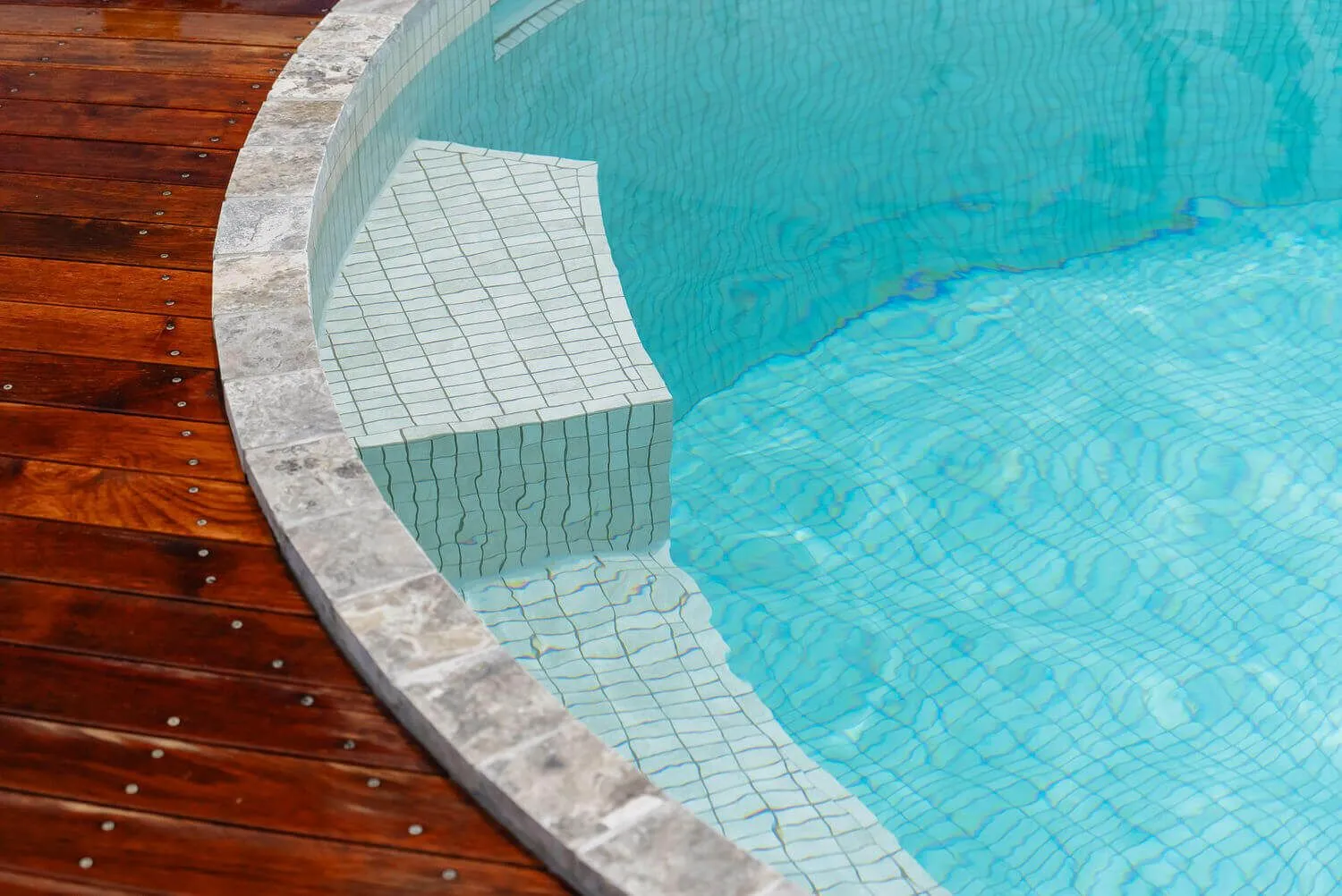 Close-up of a round plunge pool's tiled seat beside a timber deck
