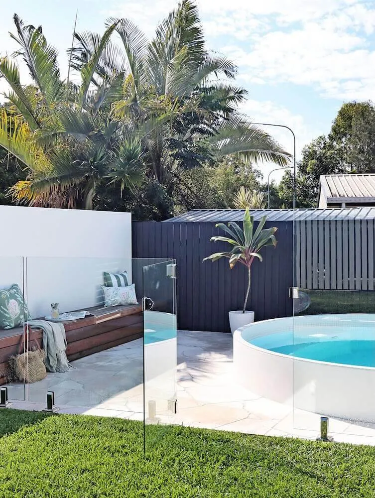 Round white plunge pool behind glass fencing in a modern courtyard