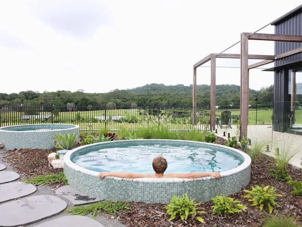 Man relaxing in a round mosaic-tiled plunge pool in a garden