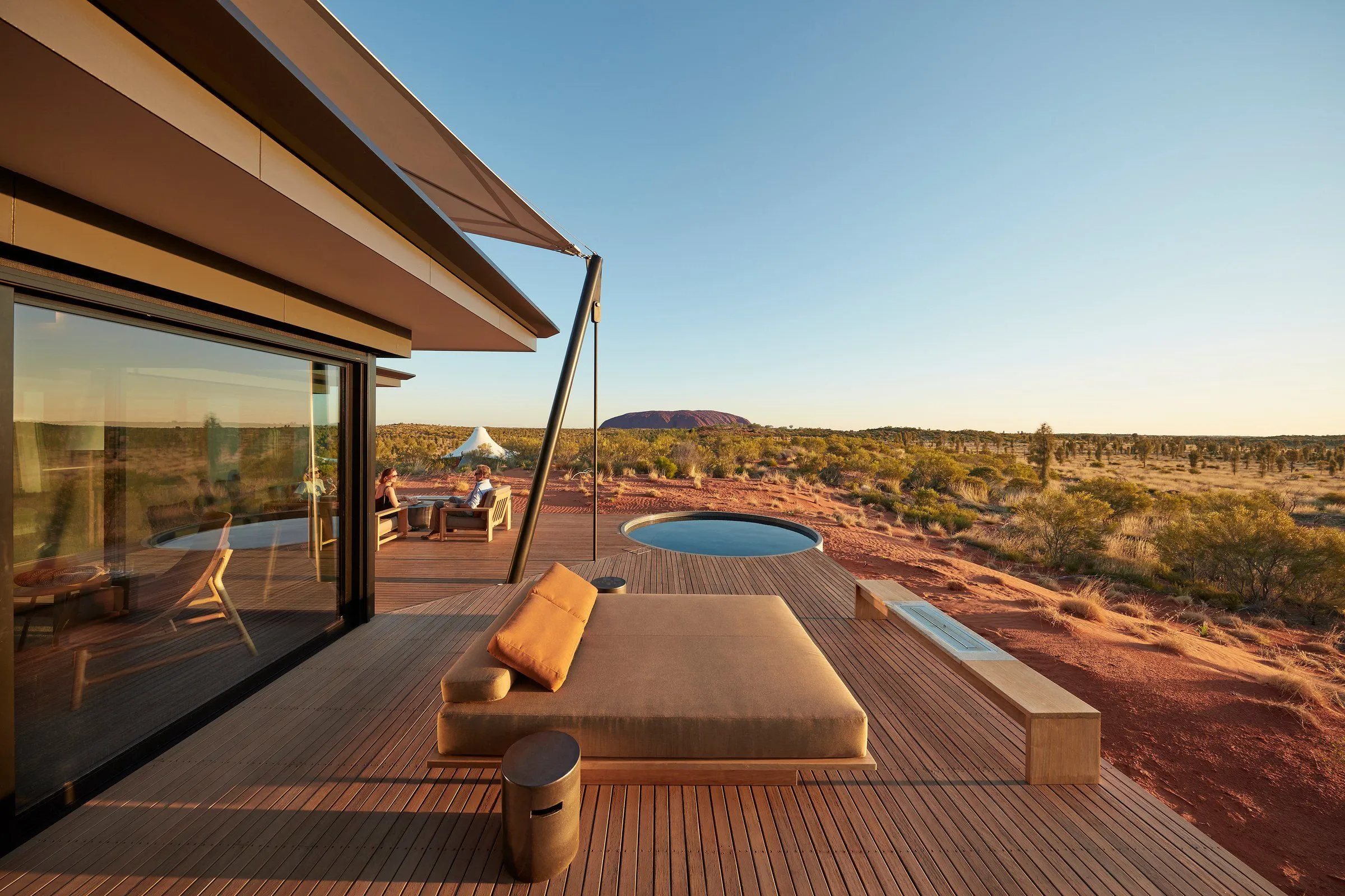 Timber deck with an outdoor daybed and a round plunge pool overlooking the red desert and Uluru