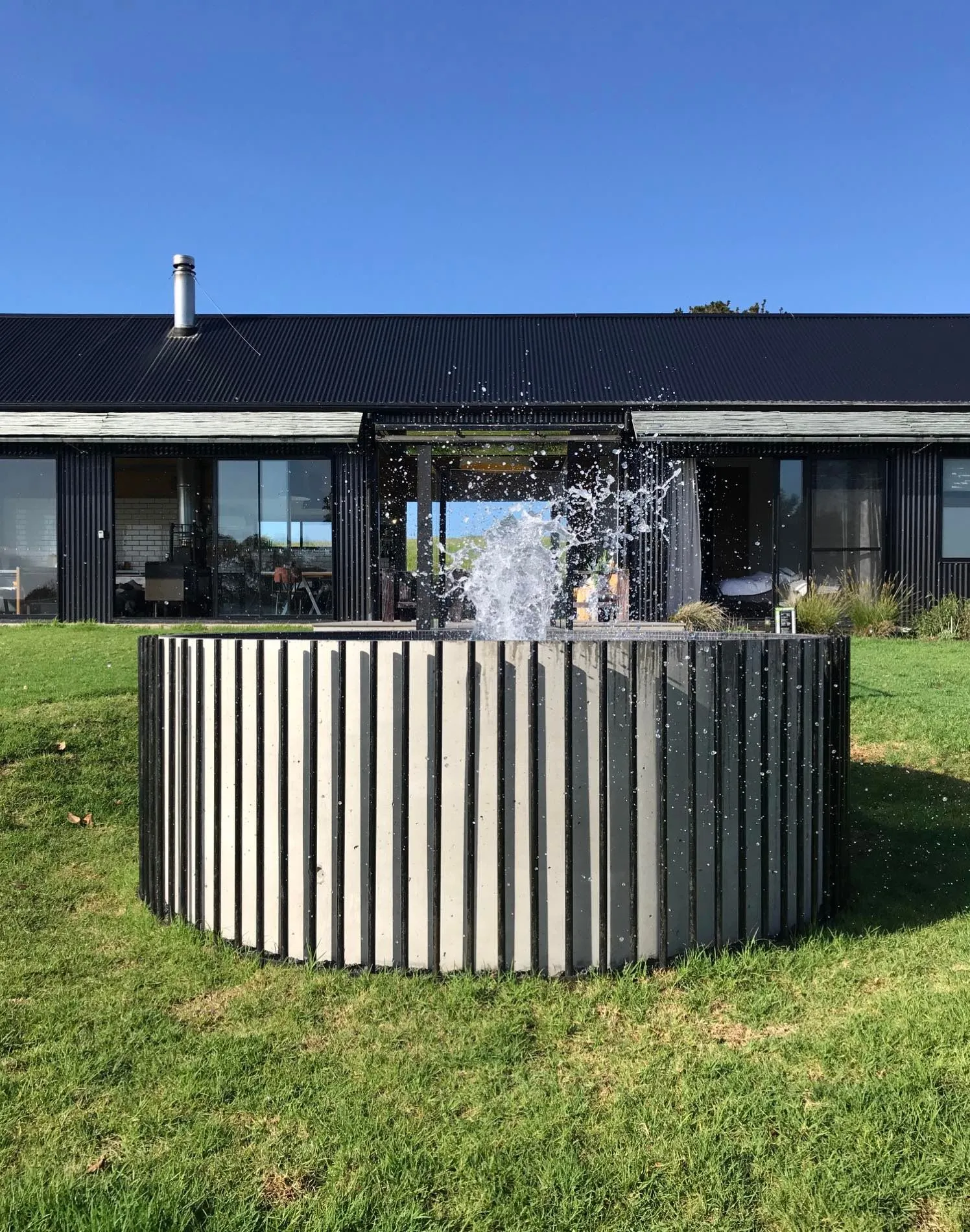 Round timber-battened plunge pool with a water feature on a lawn